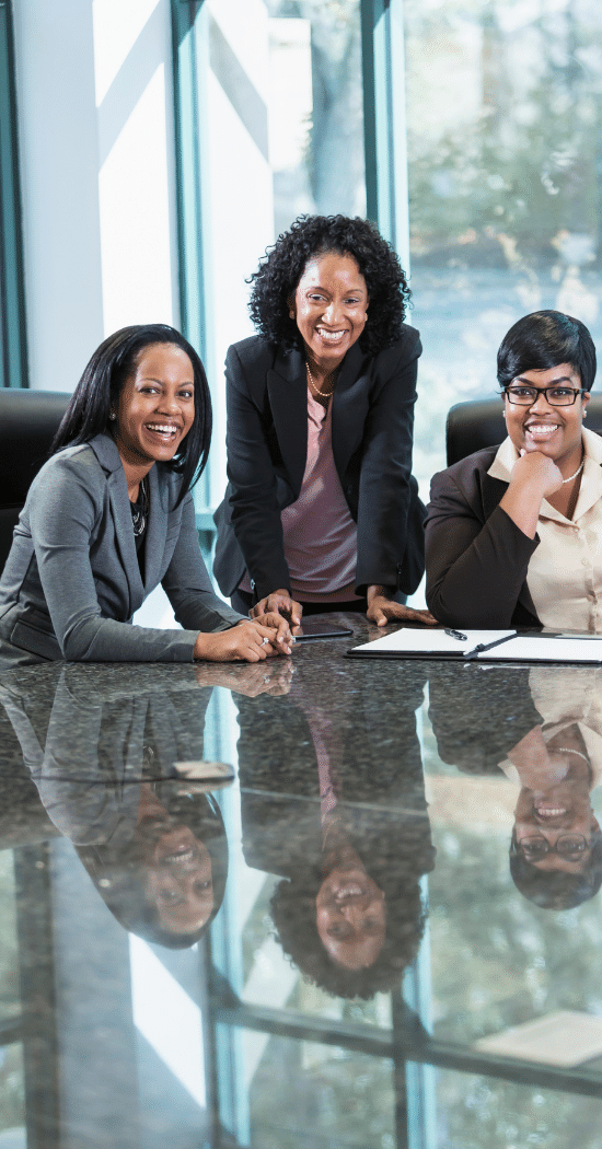 three black women sitting at a conference meeting table smiling. Scion Executive Search Foundations.