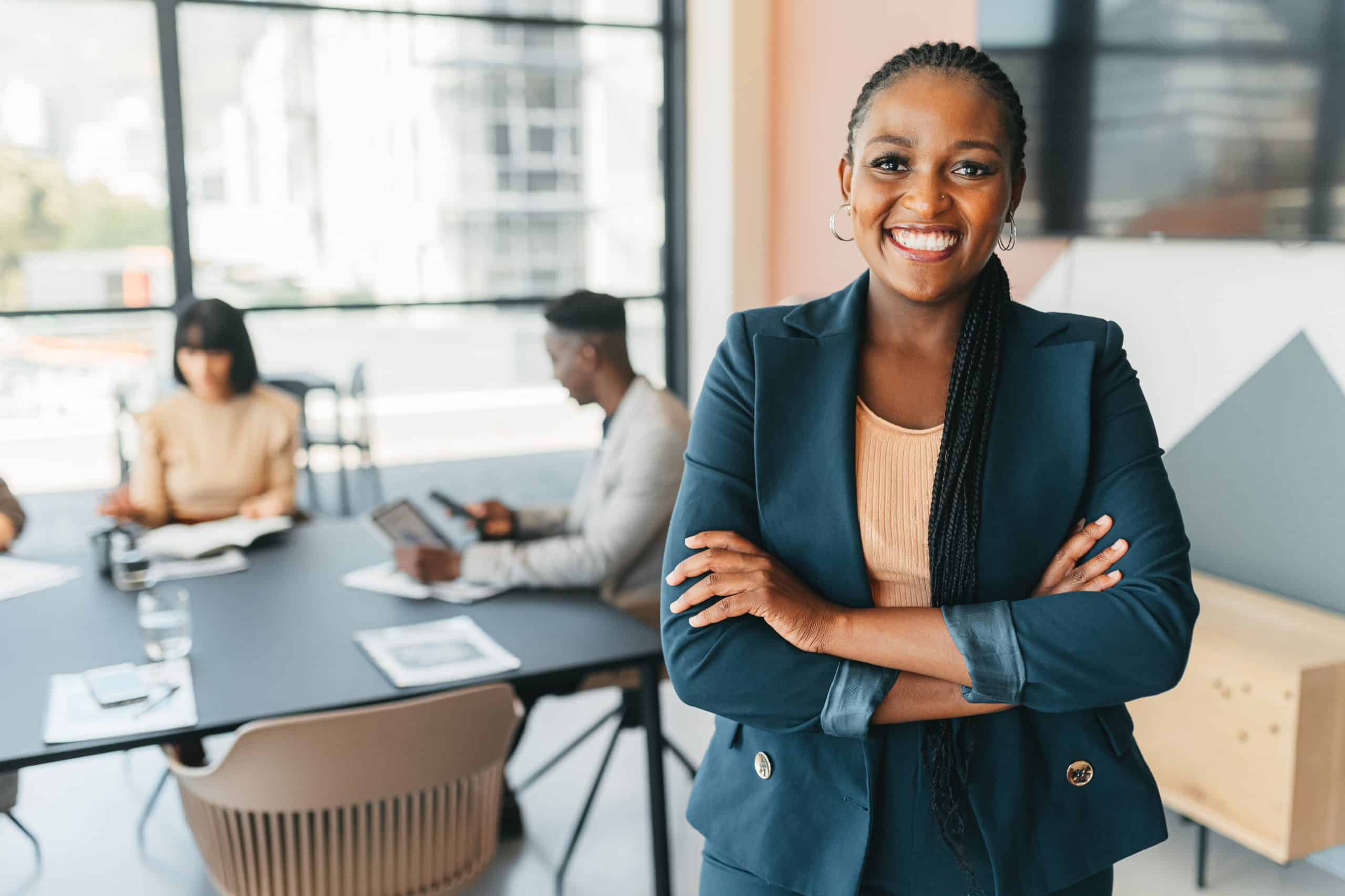 Scion Executive Search Leader, manager and CEO with a business woman in the office with her team in the background. Portrait of a female boss standing arms crossed at work during a meeting for planning and strategy